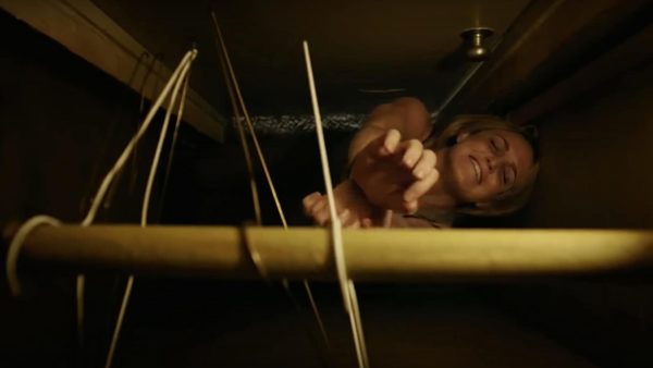 Caity Lotz, her hands bound, reaches up for a wire hanger in a closet high above