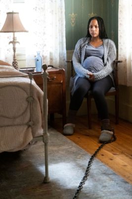 A pregnant woman sitting in a chair is chained by the foot 