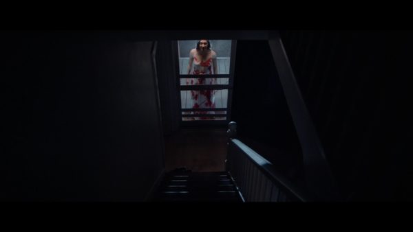 Abby (Zarah Mahler) is seen standing on the porch from a perspective at the top of the stairs