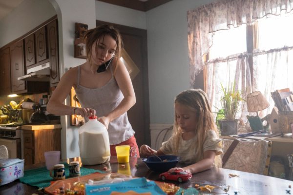 A woman on the phone opens a jug of milk for her nearby daughter