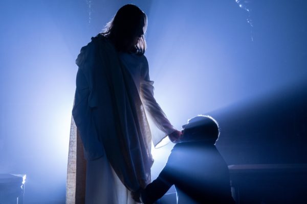 A kneeling man is touched on the chin by Jesus as light shines behind them