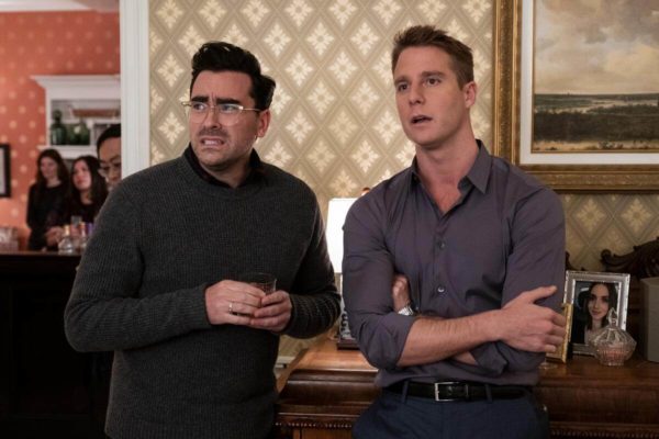 Dan Levy as John and Jake McDorman as Connor watch uncomfortably with drinks in hand
