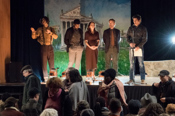 Five uncomfortable looking people stand on a stage