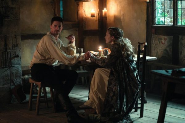 An anxious dark haired man is comforted by a blonde woman (both in Victorian-era clothes) at a table