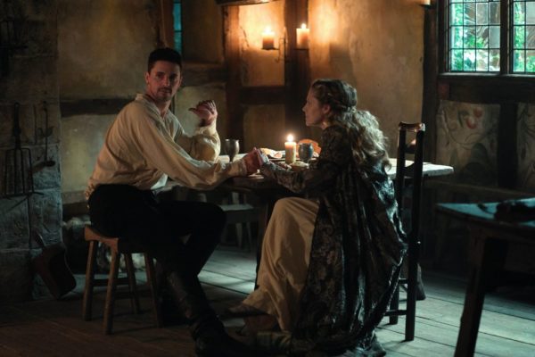 An anxious dark haired man is comforted by a blonde woman (both in Victorian-era clothes) at a table