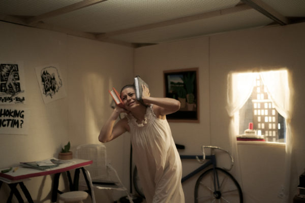 A woman with a shaved head clasps two books against her ears