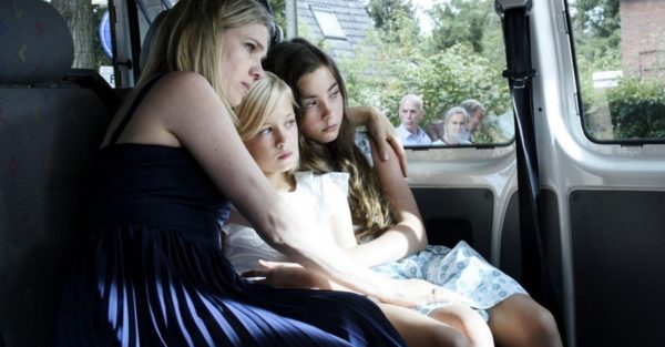 A blonde woman holds her two children in the back of a car