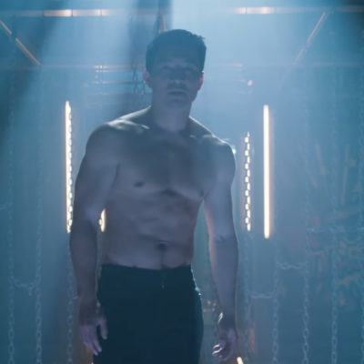 A shirtless man stands in a dimly lit space