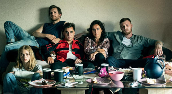 A woman sits on a couch with three men and a teen girl (far left)