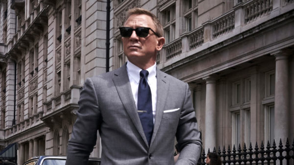 A suave blonde man in a grey suit and sunglasses 