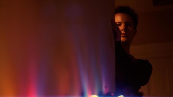 A man peer around the corner of a wall illuminated by Christmas lights