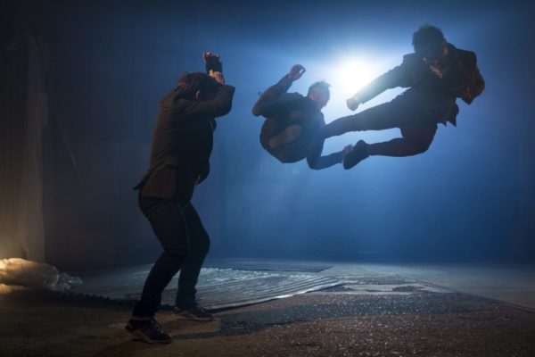 A man kicks another man in mid-air as a third man watches