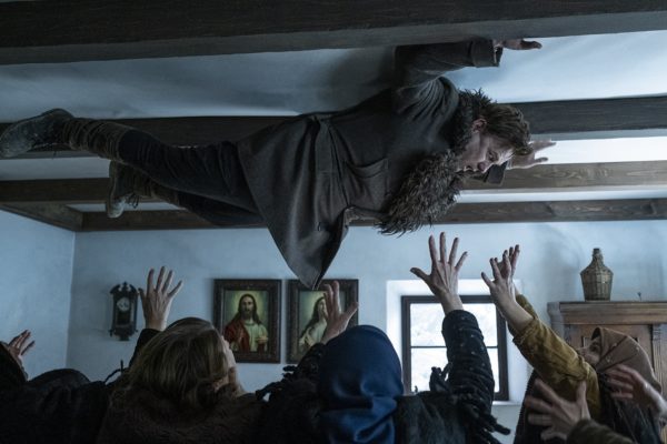 A man is pinned to the ceiling as people reach for him