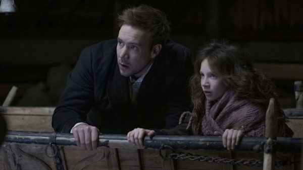 A man with dark hair clutches a railing next to a young girl