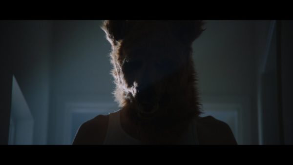 A man wearing a bear head stands in shadow