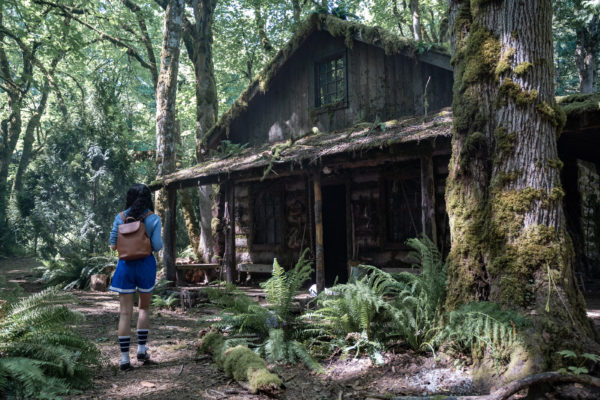 A teen girl approaches a cabin in the woods