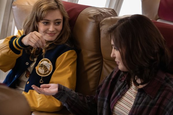 A teen girl in a leather jacket gives her brunette girlfriend a necklace