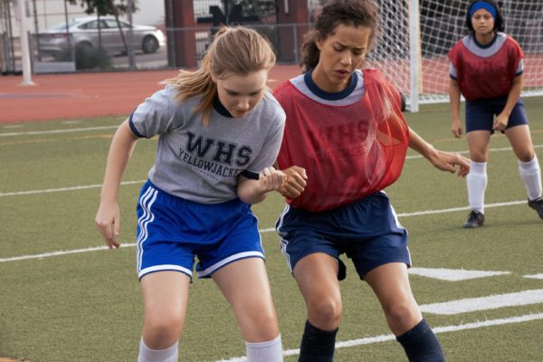 Two teen girls jostle for position on the soccer field