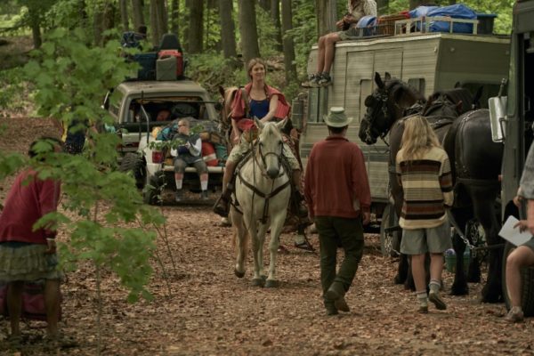 A woman on horseback next to a caravan in the woods