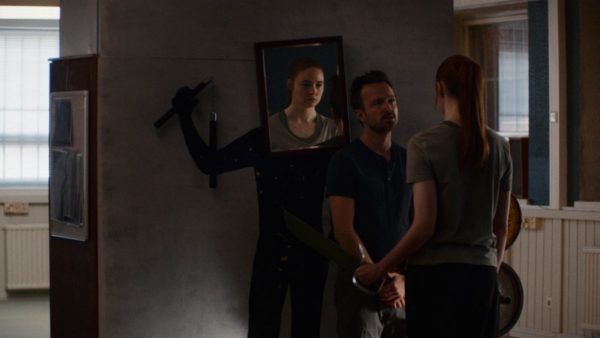 A man holds a red headed woman's wrists as she stares into a mirror