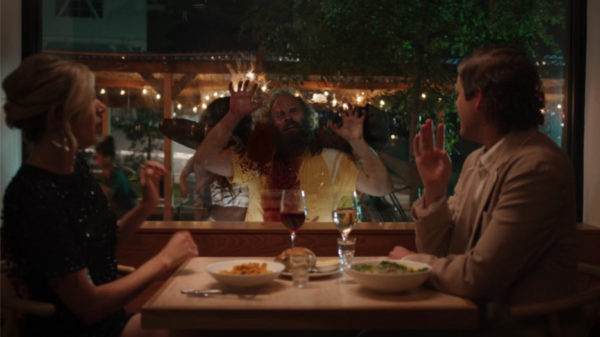 A heterosexual couple eating in a restaurant with a bleeding man pounding on the glass between them