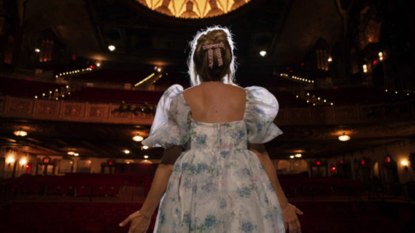 A blonde woman in a puffy dress performs for an empty theatre