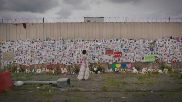 A woman in a wedding dress stands in front of a memorial wall