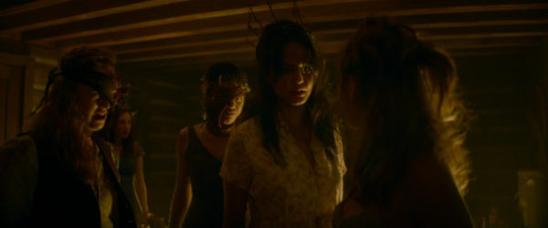 A brunette teen girl flanked by two other girls in a dimly lit cabin