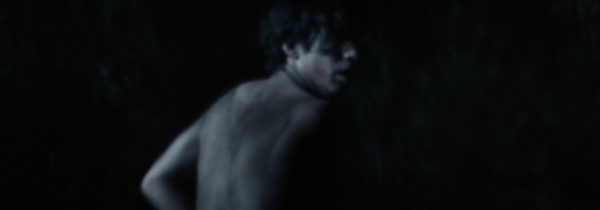 A topless teen boy running through the woods