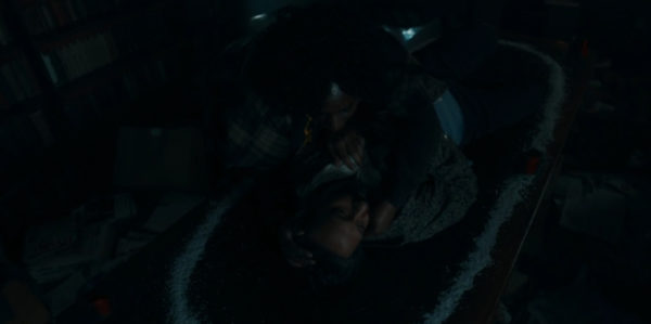 A black woman cradles a dead man in the center of a table