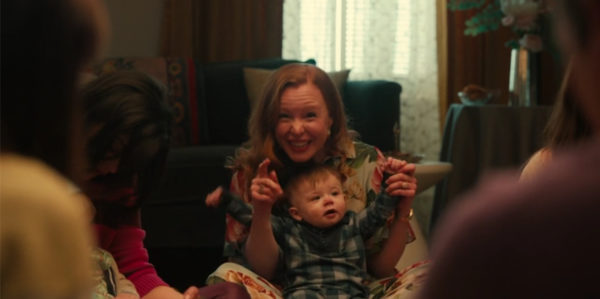 A red headed woman with a baby in her lap gesturing excitedly