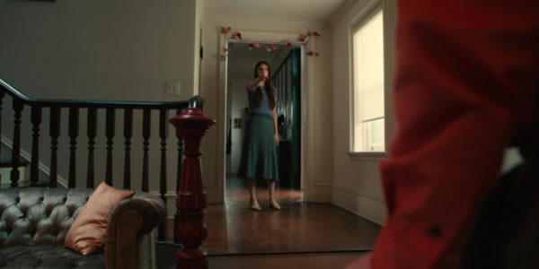 A dark haired woman holds a knife in a hallway