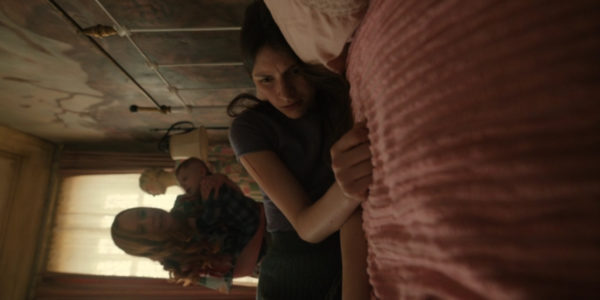 A woman lying on a bed, but the shot is flipped on its side so she looks vertical