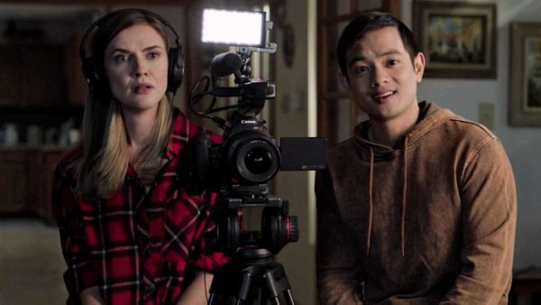 A blonde woman (L) and and Asian man (R) sit on either side of a professional camera