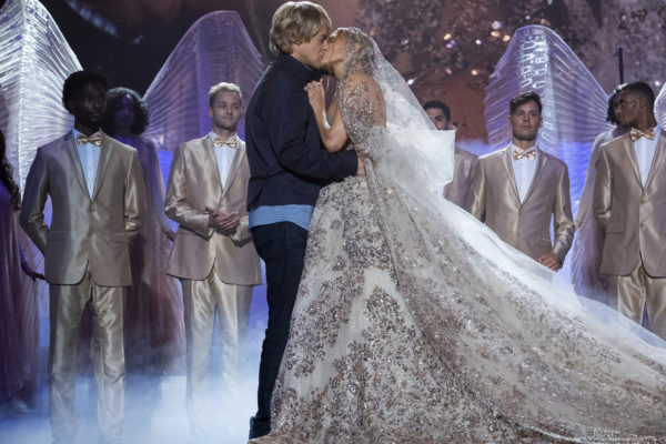 A plainclothes man (L) kisses a woman (r) in an extravagant wedding dress on stage
