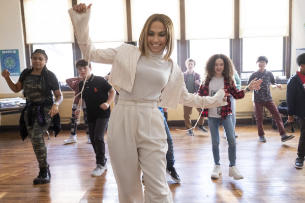 A woman in white dances in front of a row of pre-teens