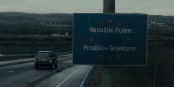 A car driving past a sign indicating they're arriving in Poland