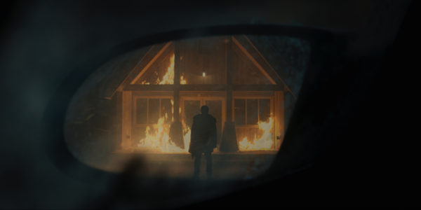 A man stands in front of a burning burning, as seen through the window of a vehicle