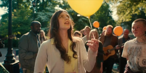A brunette holds a yellow balloon in the park