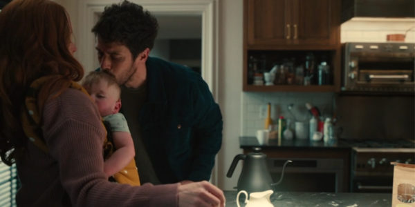 A man kissing the top of a baby's head as the woman holding it leans away