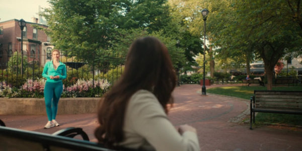 A woman in a blue jumpsuit looks at a crying woman on a park bench