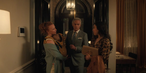 A redheaded woman with a baby greets an older white man and a young brunette in the foyer