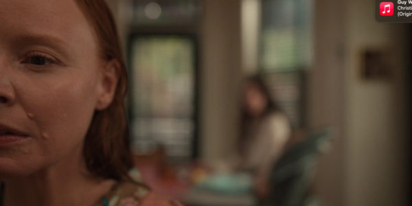 Half of a red headed woman's face (in foreground) with a dark haired woman sitting at the table behind her