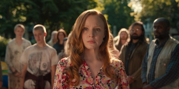 A red headed woman surrounded by people in a sunny park