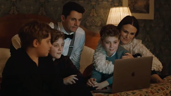 A dressed up family gathered on a bed smiles at a computer