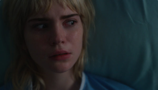 A close-up of a scared blonde girl's face in a hospital bed