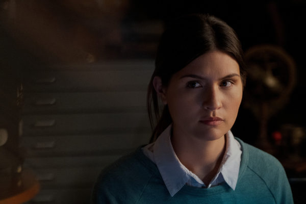 A brunette woman wearing a blue sweater and white collared shirt