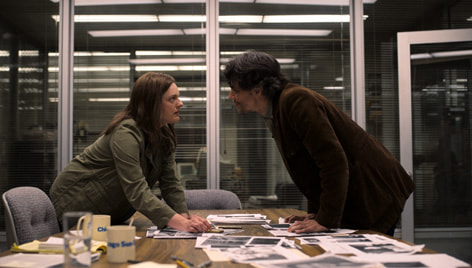 A man (R) and woman (L) lean over a table of evidence