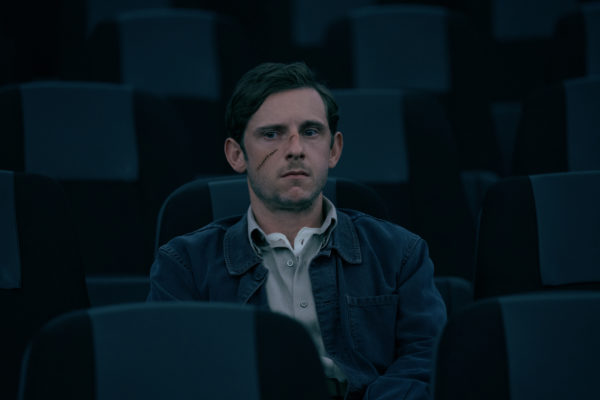 A man with a scarred face sits in an auditorium