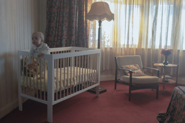 A baby stands in a crib (L)
